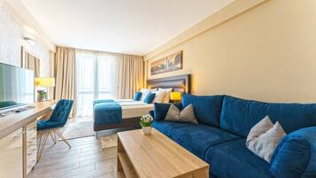 A modern hotel room with a wooden desk, a blue sofa, a bed with matching pillows, and a cityscape painting on the wall.