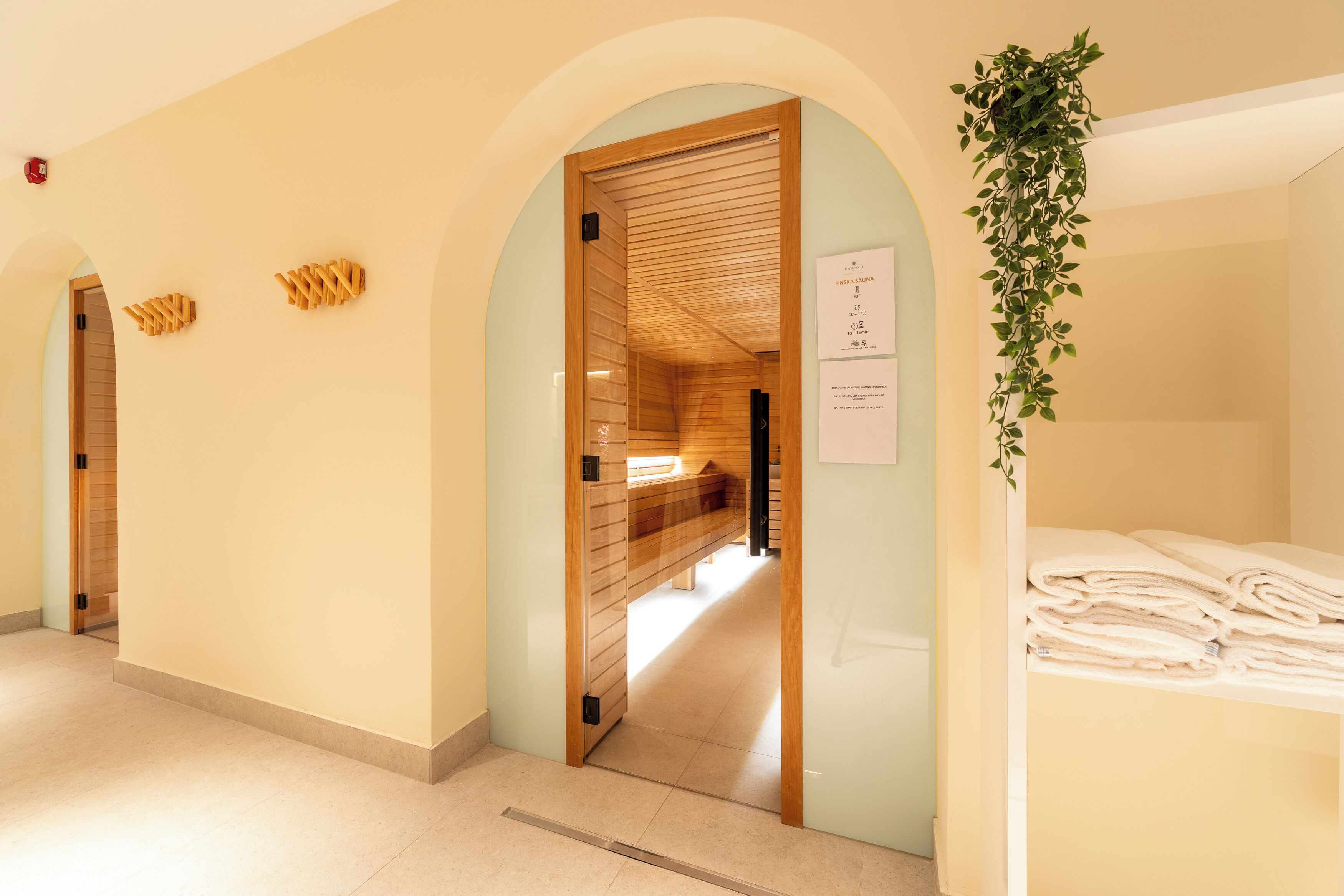 Corredor de hotel com portas de madeira, um banco e uma planta.