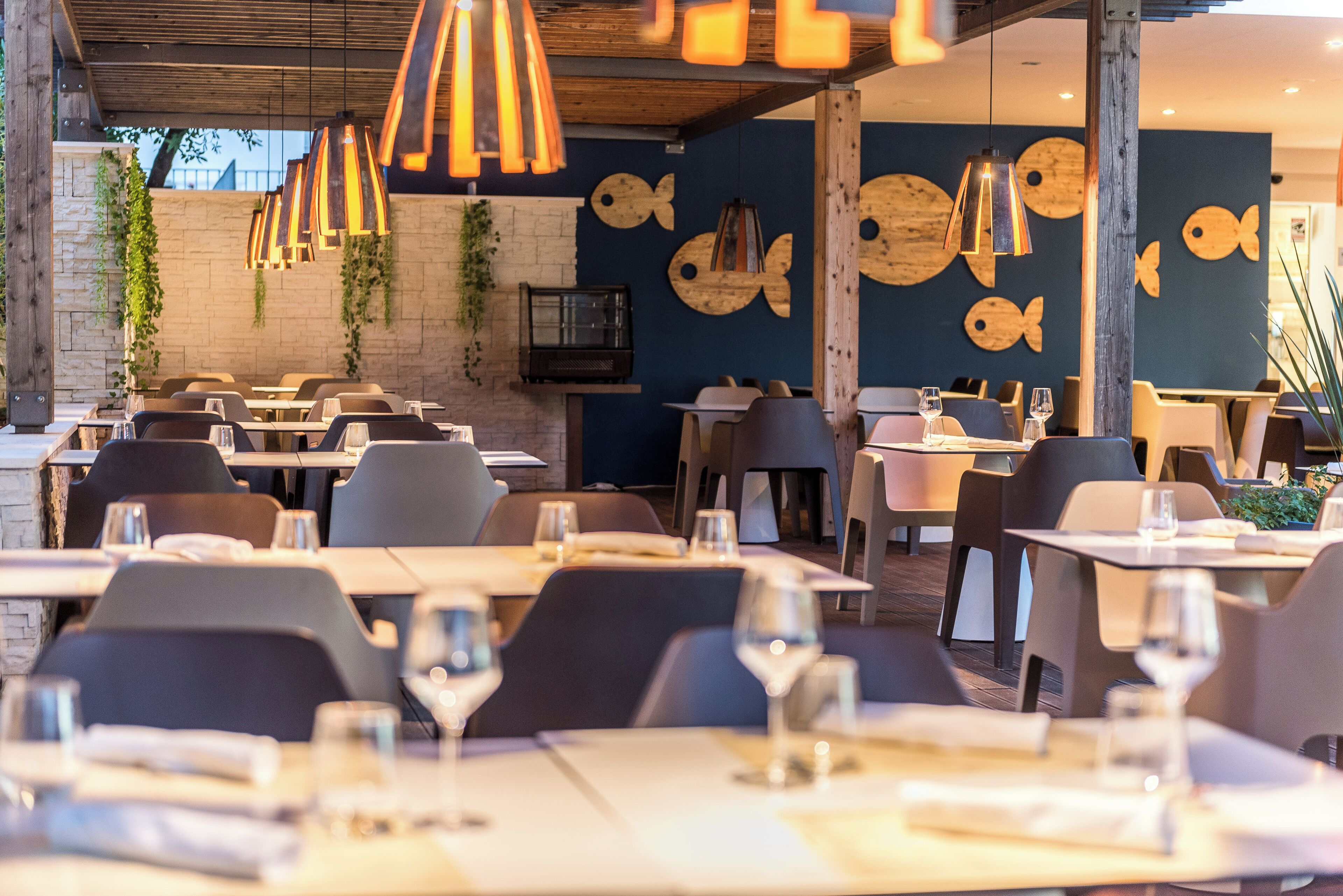 Een restaurant met meerdere tafels en stoelen, houten balken in het plafond en decoratieve muren met vismotieven.
