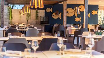 Een restaurant met meerdere tafels en stoelen, houten balken in het plafond en decoratieve muren met vismotieven.