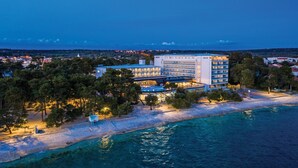 Un hôtel situé sur la côte, doté d’un grand bâtiment, d’une plage et d’une eau cristalline.