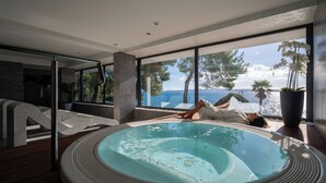 Uma área moderna com piscina interna e vista para o mar, uma banheira de hidromassagem e um espaço de estar também com vista.