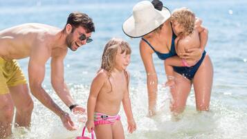 A family of four at a beach with clear water and mountains in the background.