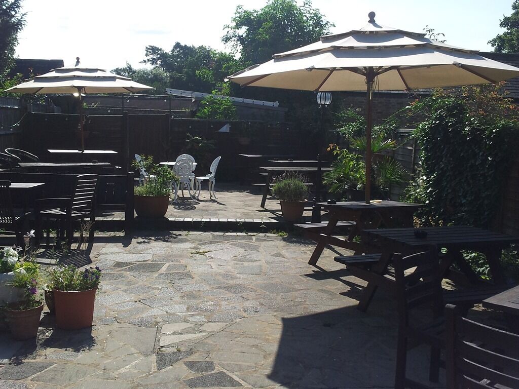An outdoor patio with stone flooring, wooden tables and chairs, and large umbrellas providing shade.