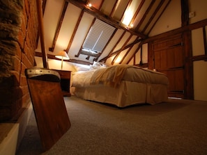 A bedroom with a sloped ceiling, a bed, a nightstand, and a lamp.