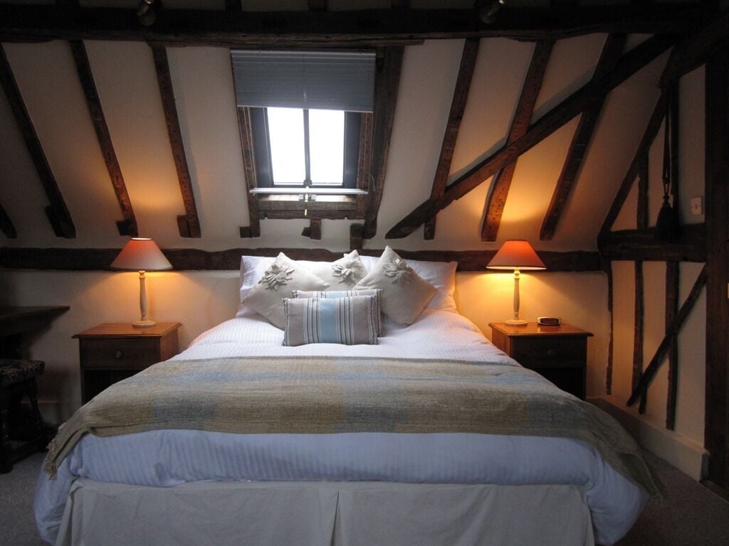 A bedroom with a large bed, two bedside lamps, and exposed wooden beams.