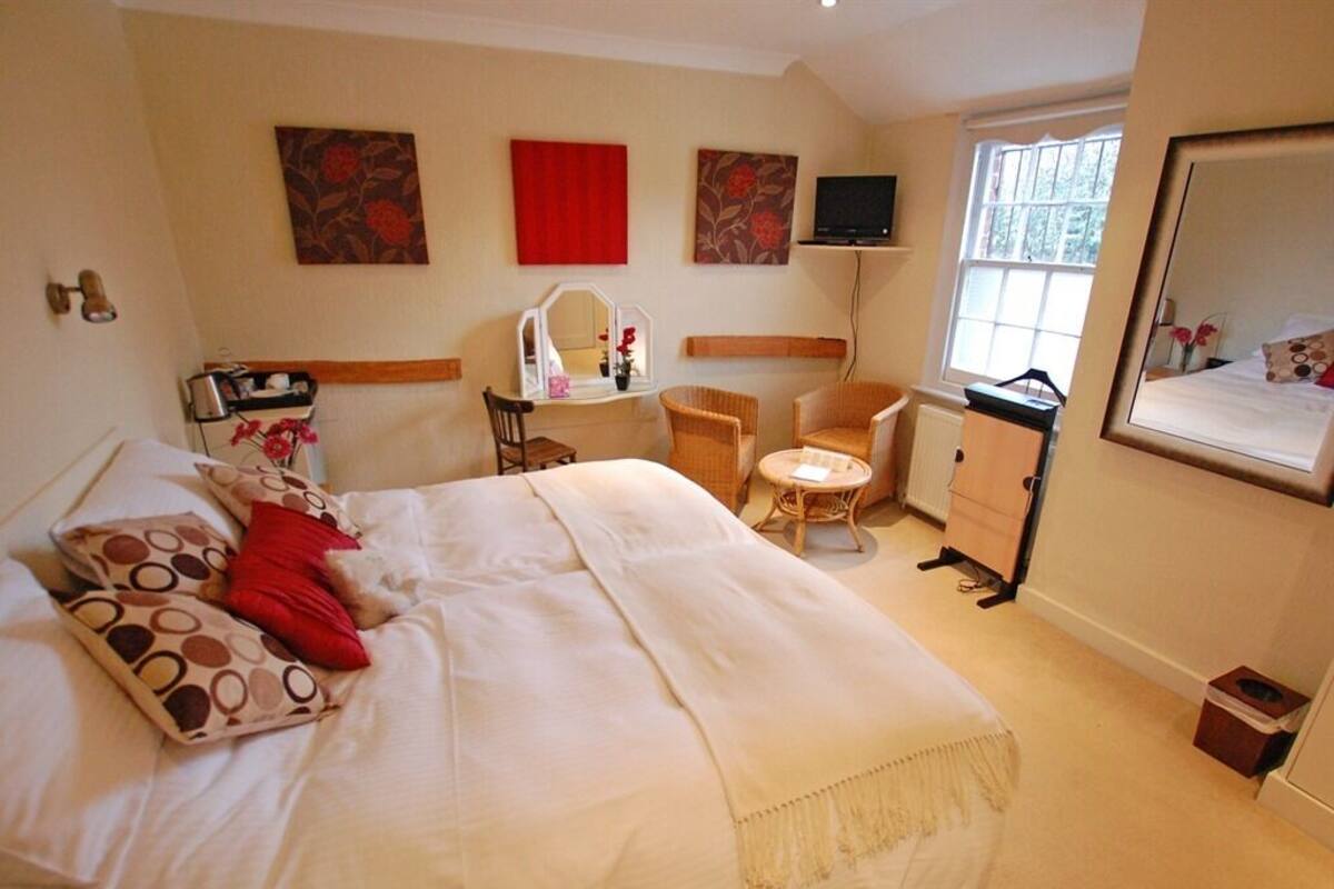 A hotel room with a large bed, a sitting area with a chair and a small table, a TV mounted on the wall, and a window providing a view of the outdoors.