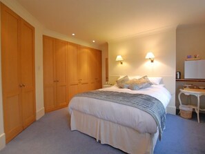A bedroom with a large bed, wooden wardrobes, two wall-mounted lamps, and a small table with a basket.