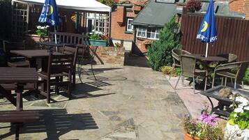 An outdoor patio area with stone flooring, wooden tables and chairs, and blue umbrellas.