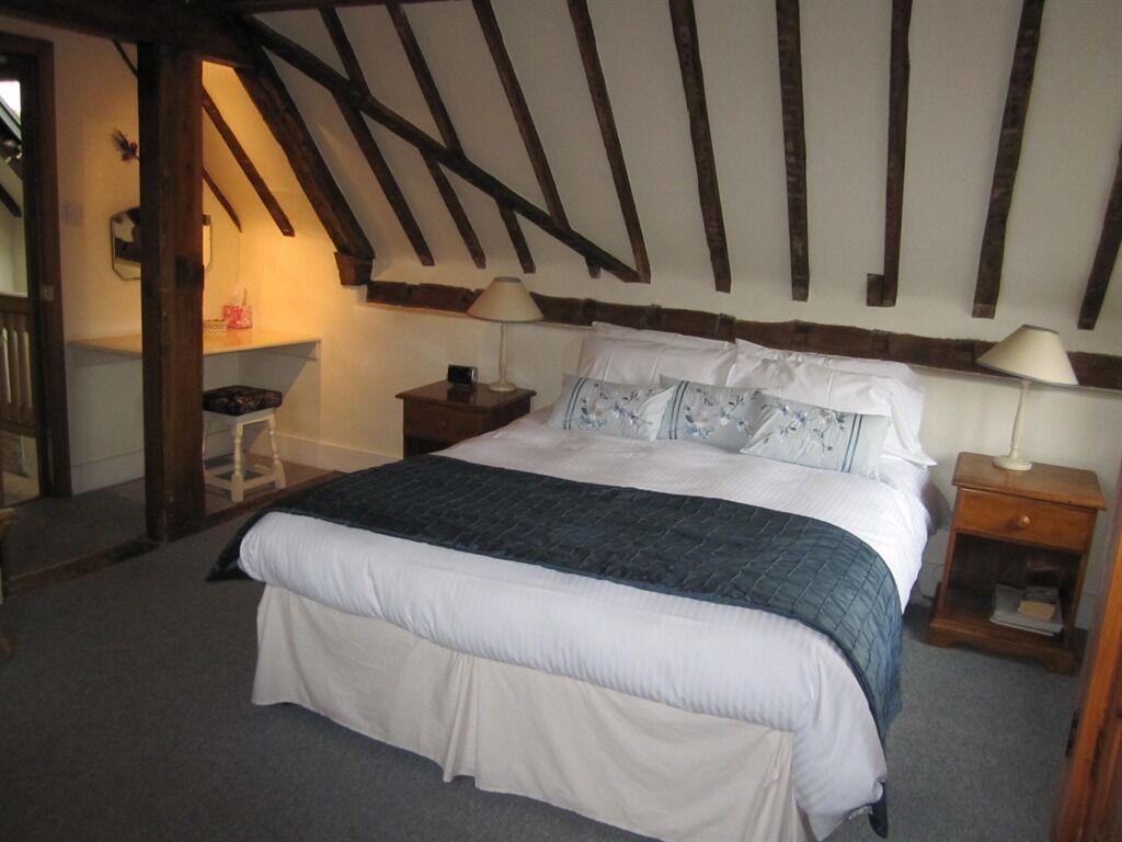 A bedroom with a large bed, wooden beams on the ceiling, two bedside tables with lamps, and a small chair.