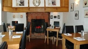 Un comedor con mesas y sillas de madera, una chimenea de ladrillo y cuadros en las paredes.