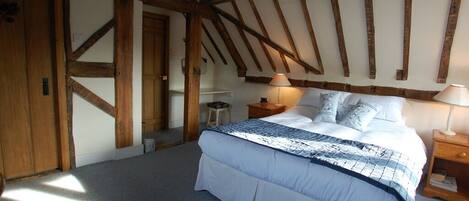A bedroom with a large bed, wooden beams, a nightstand, and a lamp.