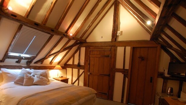 Un dormitorio con una cama grande, vigas de madera, una ventana con persianas y un armario de madera.