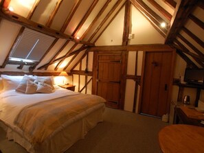 Een slaapkamer met een groot bed, houten balken, een raam met jaloezieën en een houten garderobe.