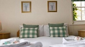 A neatly made bed with checkered pillows, a window with a view of greenery, and two framed pictures on the wall. - The Greyhound Inn Aldbury (Tring)