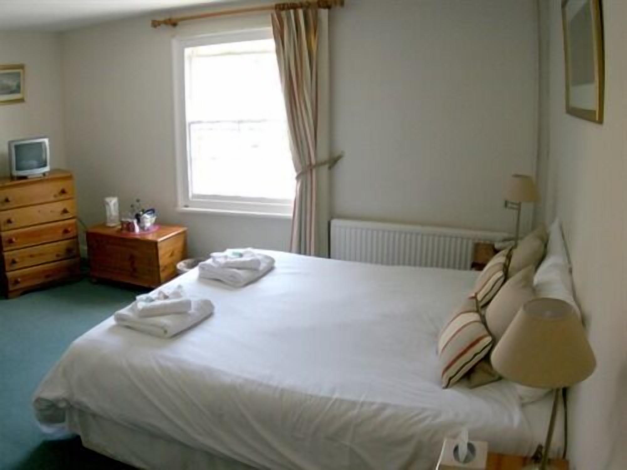 Een hotelkamer met een bed, een dressoir, een nachtkastje, een lamp en een raam met gordijnen.