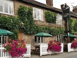 El Greyhound Inn con paredes cubiertas de hiedra, un letrero de pub tradicional y mesas al aire libre con sombrillas verdes.