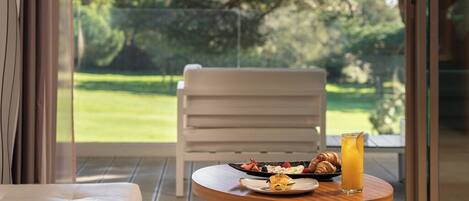 Une table à manger avec des aliments pour le petit-déjeuner et un verre de jus d’orange, le tout placé sur un balcon offrant une vue sur un paysage verdoyant.