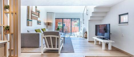 A modern living room with a sofa, chair, TV, and staircase leading to an outdoor area.