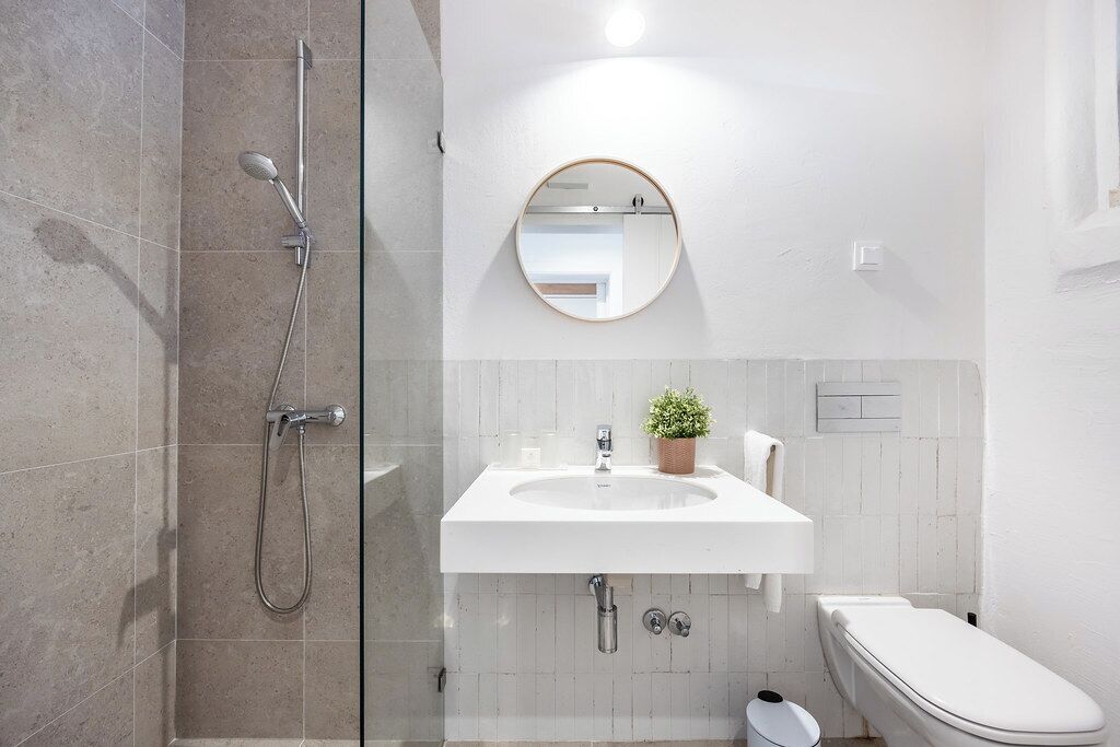 A bathroom with a glass shower enclosure, a white sink with a mirror above it, and a toilet.