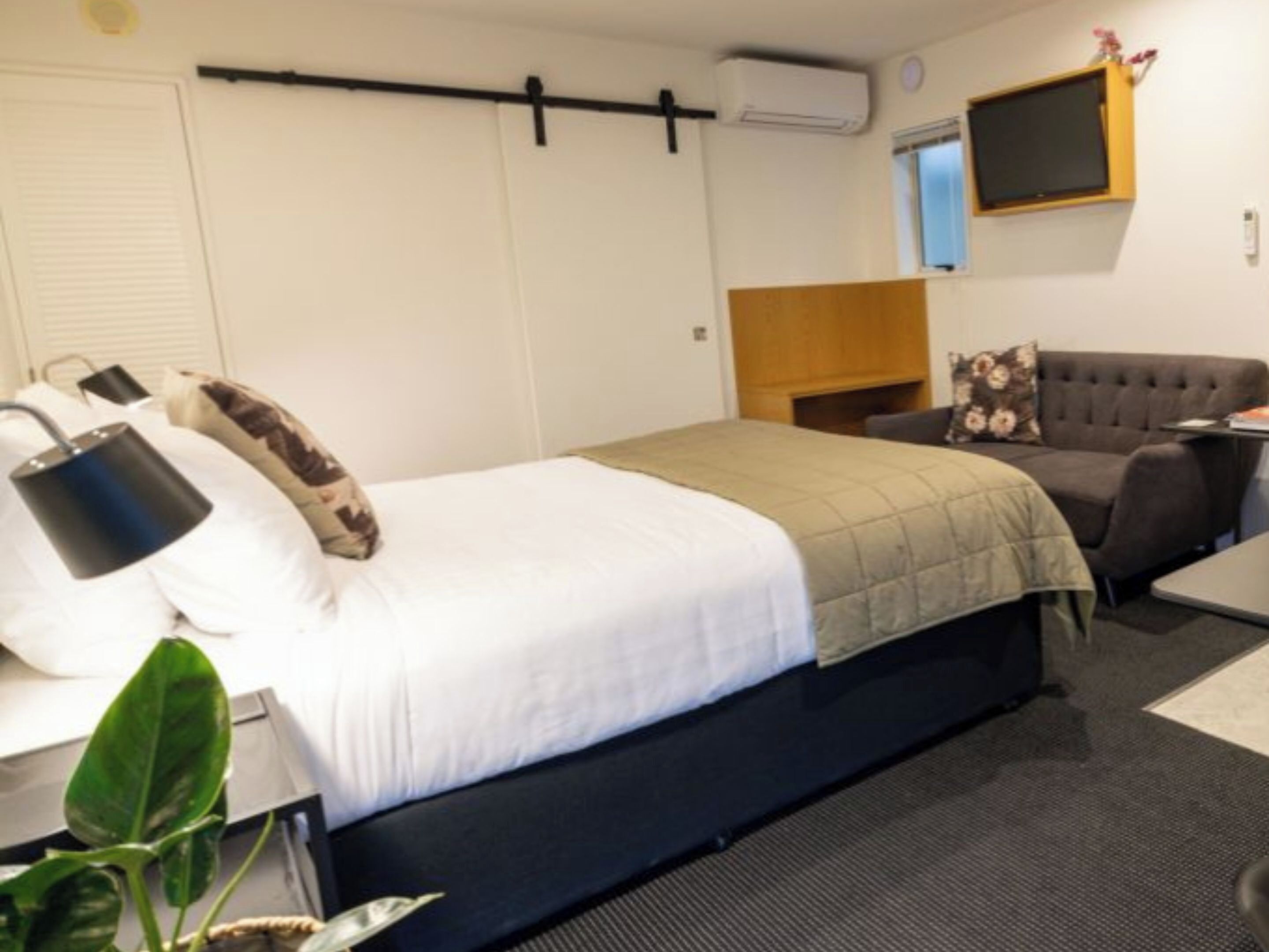 Een hotelkamer met een bed, een bureau met lamp, een bank, een televisie en een plant.