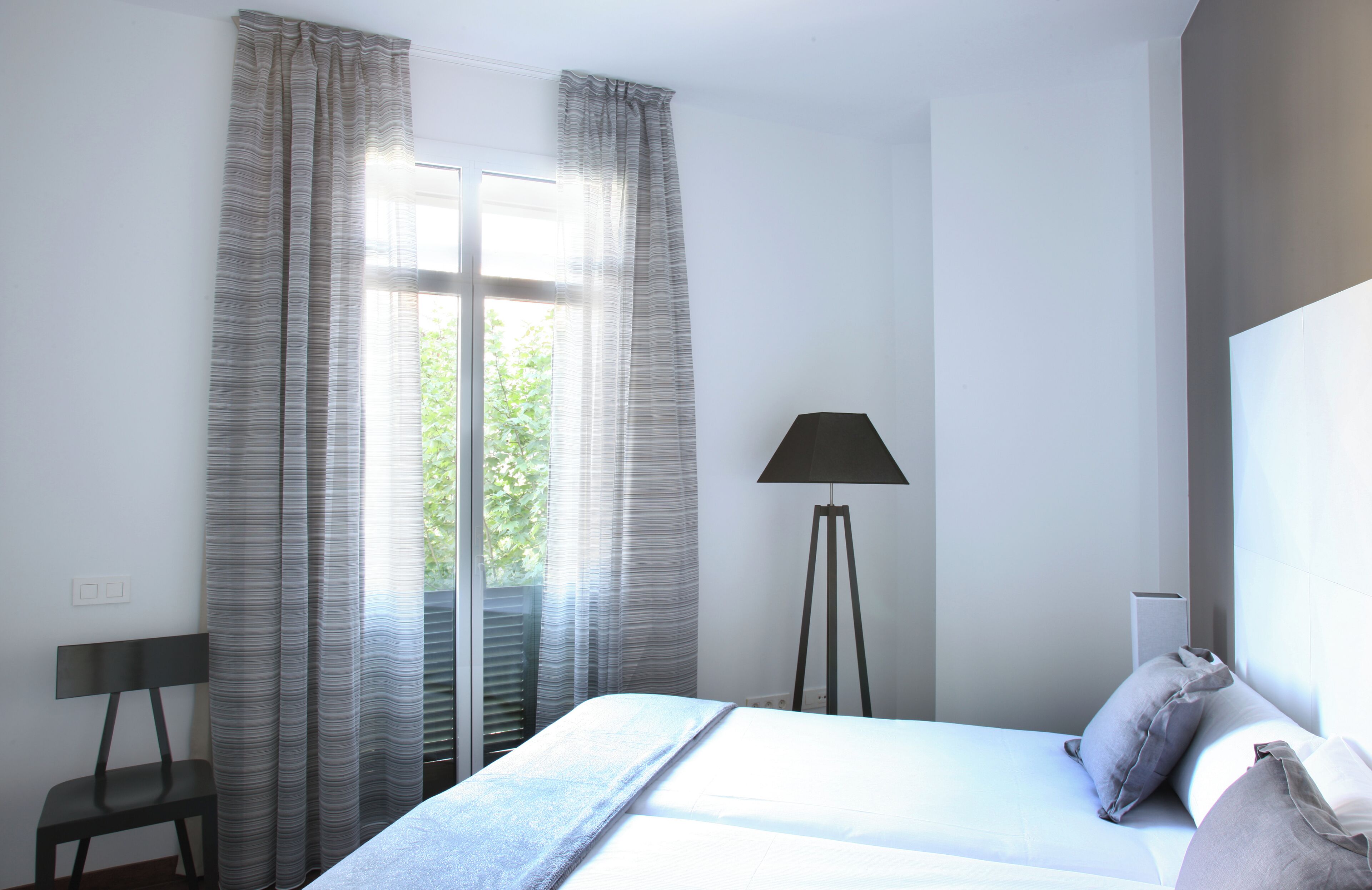 Une chambre moderne avec un grand lit, une chaise, une lampe sur pied et une fenêtre avec des rideaux.