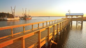 Un muelle de madera se adentra en aguas tranquilas, con barcos amarrados cerca y una estructura cubierta al final.