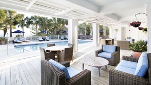 A covered outdoor area with a pool, wicker furniture, and hanging flower baskets. - The Cottages on Charleston Harbor (Mount Pleasant)