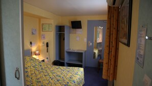 Una habitación de hotel con una cama, un escritorio, una silla, un televisor y una puerta.