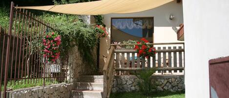 A stone staircase leading to a wooden door, surrounded by a metal fence and a tan awning.