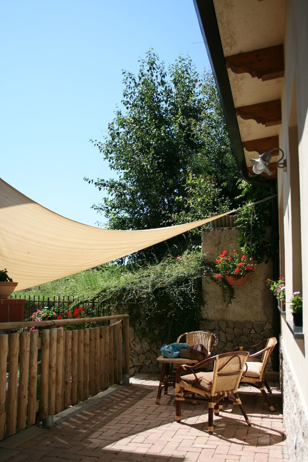 An outdoor patio area with a wooden fence, two wicker chairs, a table, and a beige shade sail.