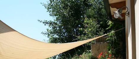 An outdoor patio area with a wooden fence, two wicker chairs, a table, and a beige shade sail.