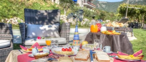 Una preparación para el desayuno sobre una mesa con mantel rojo, que incluye platos de comida, bebidas y un jarrón con una rosa azul.