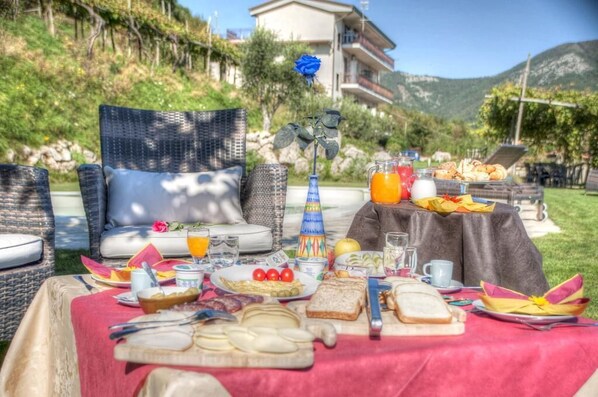 A breakfast setup on a table with a red tablecloth, including plates of food, drinks, and a vase with a blue rose. - Casa Pendola (Agerola)