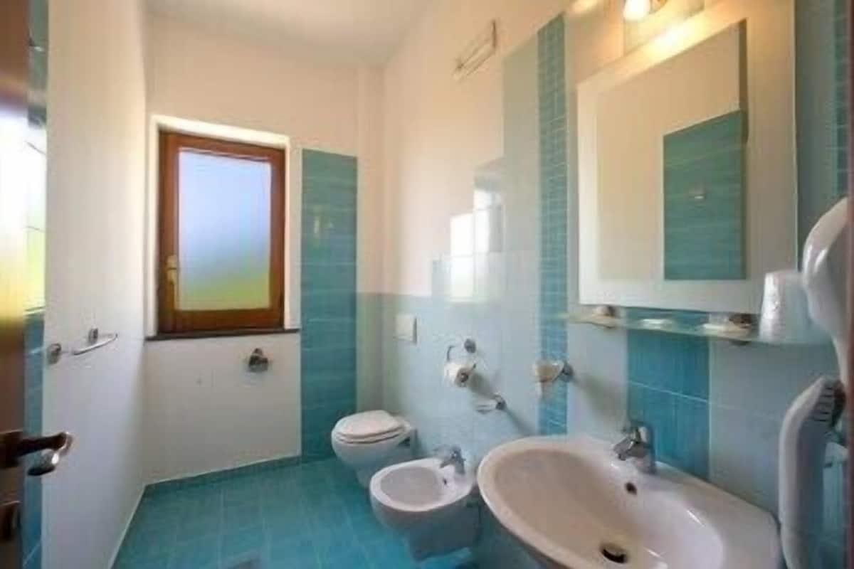 A bathroom with a toilet, bidet, and sink, featuring blue tiles and a window.