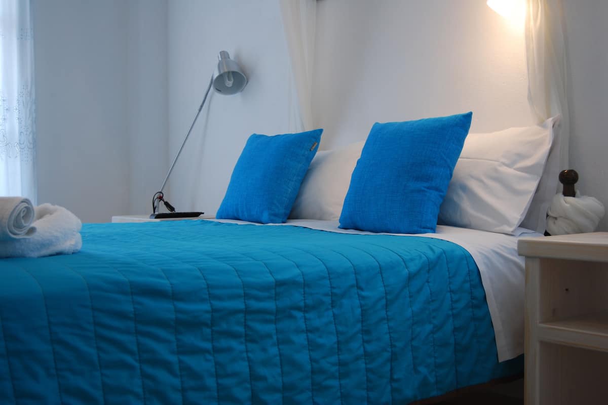 A neatly made bed with a blue quilt, white pillows, and a white headboard.