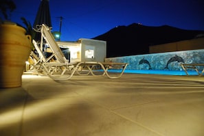 A poolside area with lounge chairs, a small building, and a stone wall with dolphins.