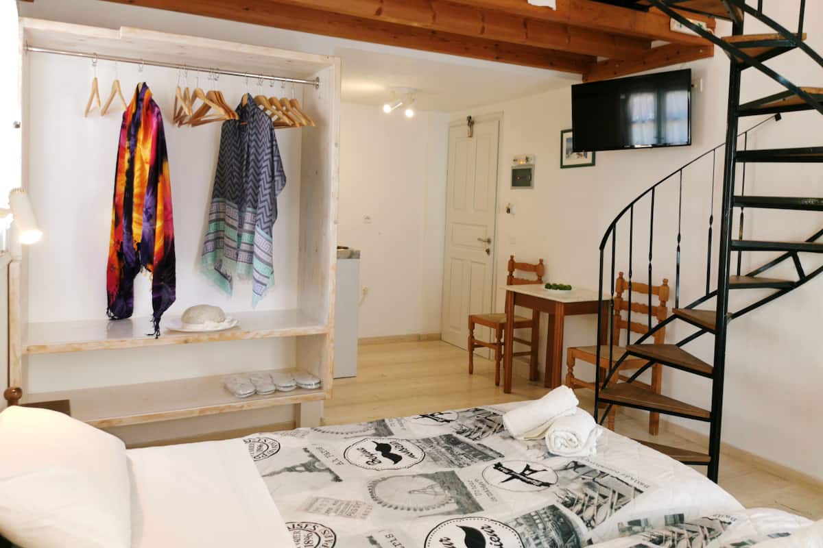 A bedroom with a bed, a wooden wardrobe, a spiral staircase, and a dining area.