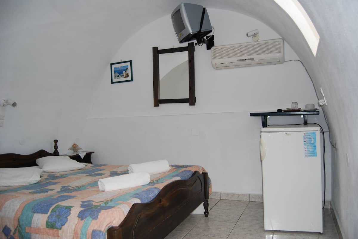 A bedroom with a bed, a small white refrigerator, a television mounted on the wall, and a picture frame.