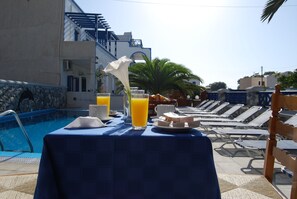 Desayuno junto a la piscina con una mesa, sillas y una pileta.