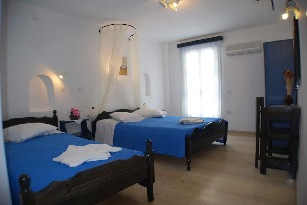 A bedroom with two beds, a wooden floor, a nightstand with a lamp, and a window with curtains.