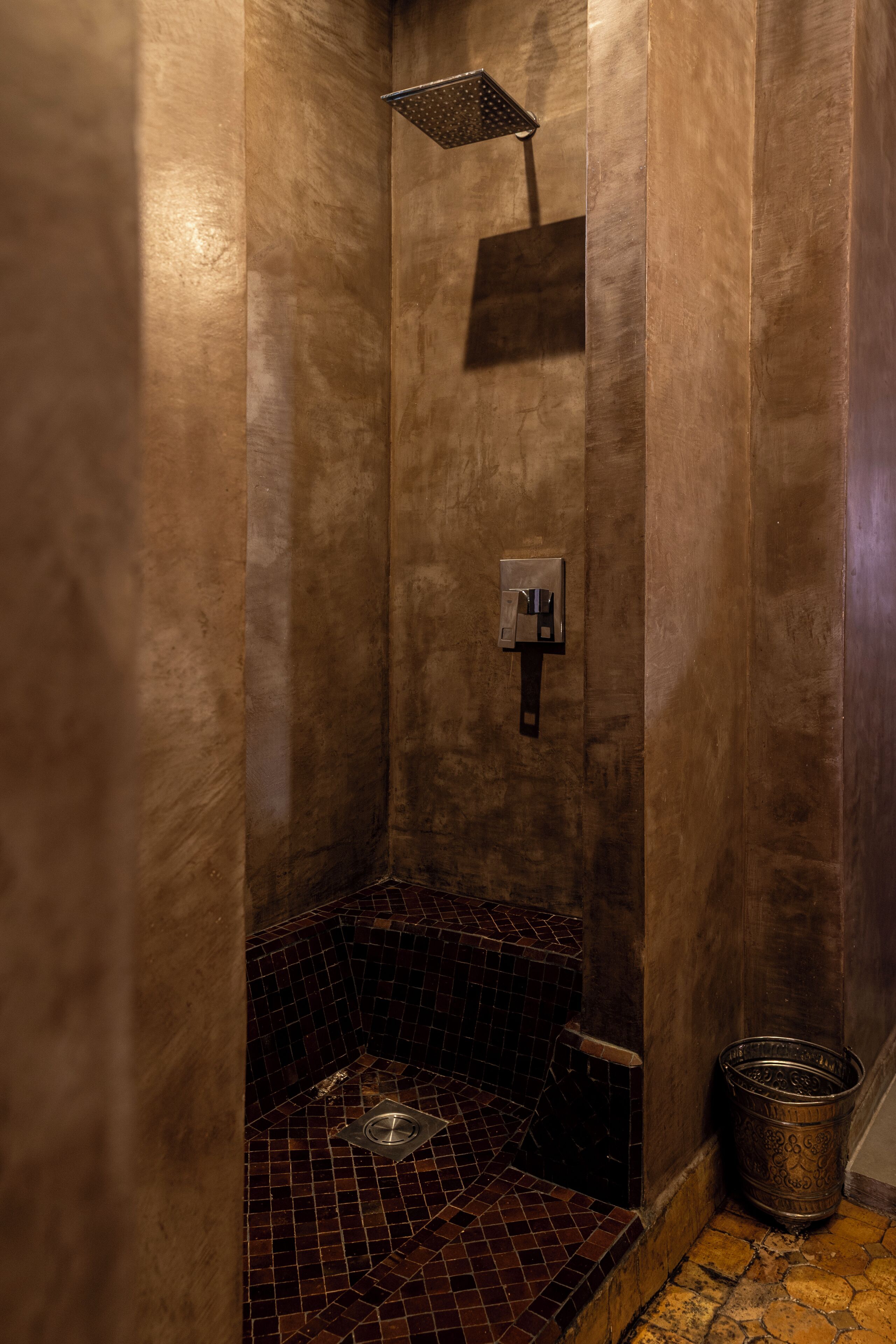 A small, tiled shower area with a showerhead and a metal bucket.