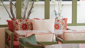 A cozy seating area with cushioned chairs and a table, adorned with patterned cushions, under a wooden ceiling with hanging lanterns.