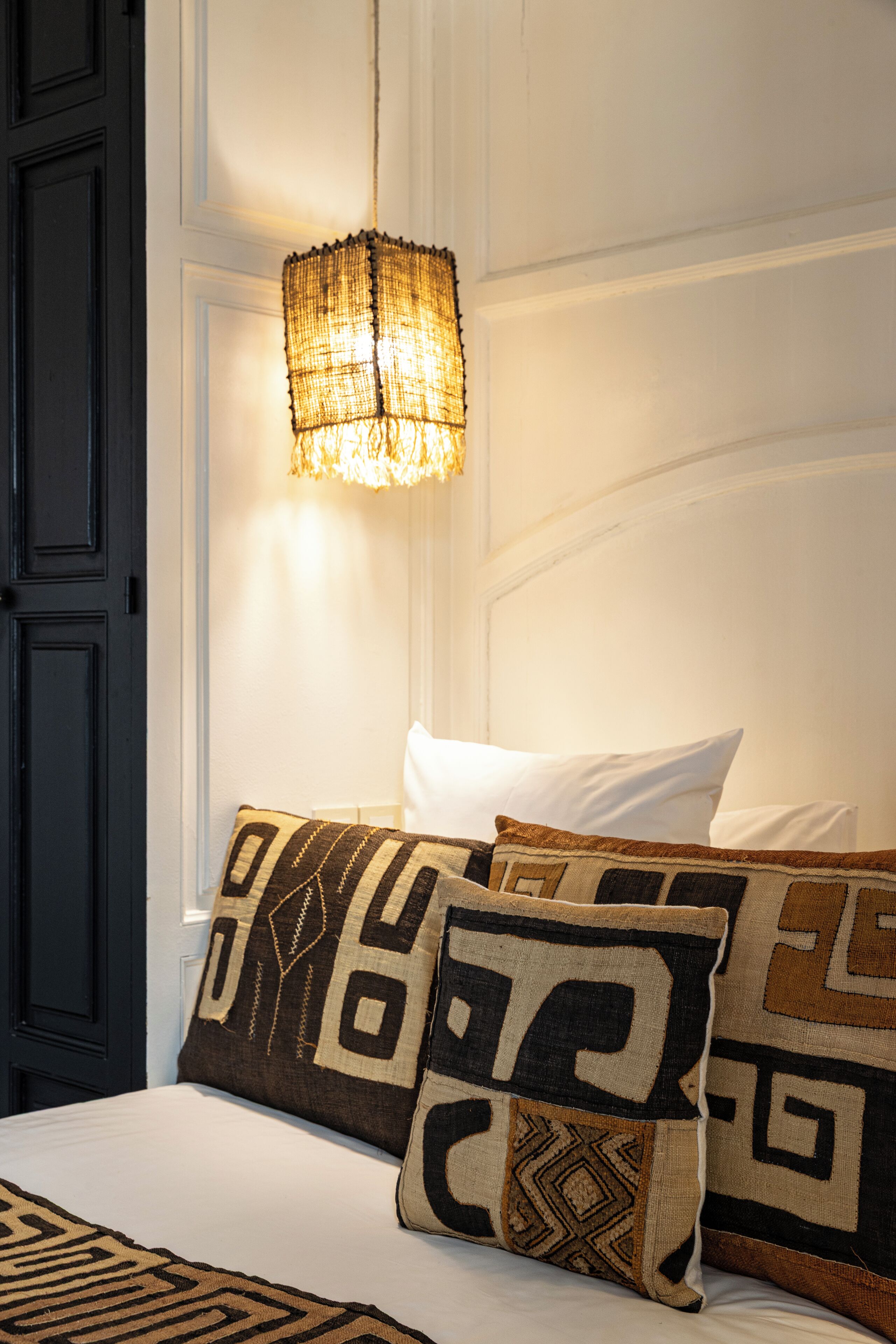 A bed with patterned pillows and a hanging light fixture.