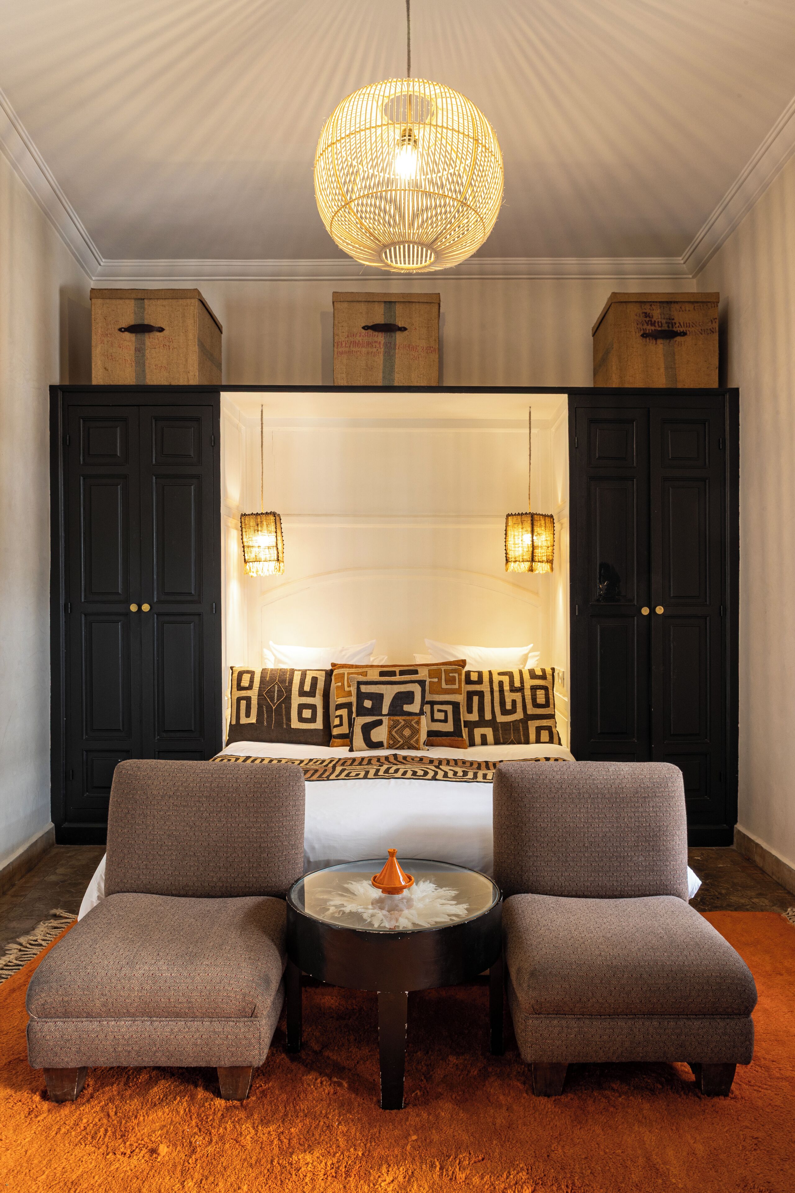 A modern room with a bed, two armchairs, a round table, and a large hanging light fixture.