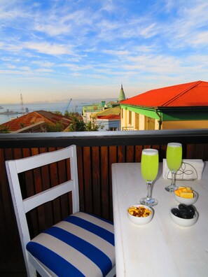 A balcony with a view of a cityscape, including a bridge and buildings. There is a table with two glasses of green drink and a bowl of snacks. - Montealegre (Valparaiso)
