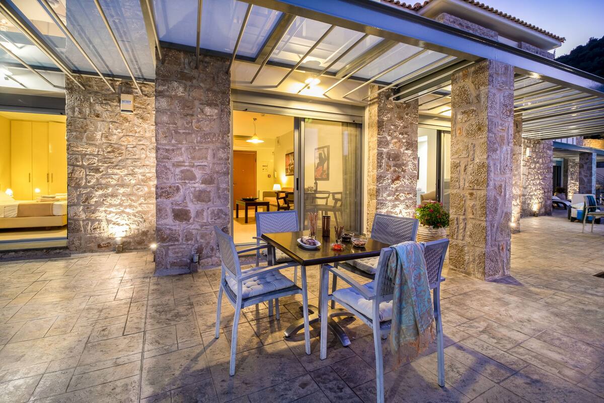 An outdoor patio with stone pillars, a glass door leading to an interior room, and a table set for dining.