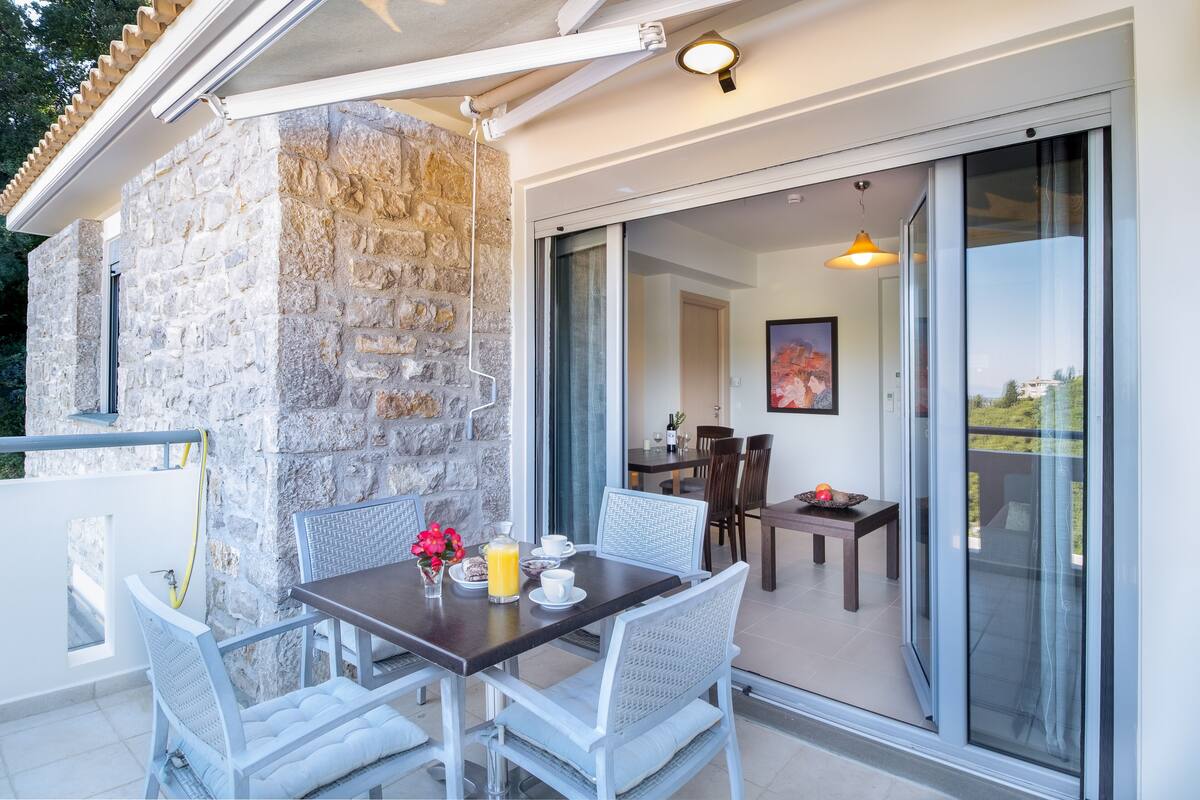 An outdoor dining area with a stone wall, a table with chairs, and a view of the interior through glass doors.