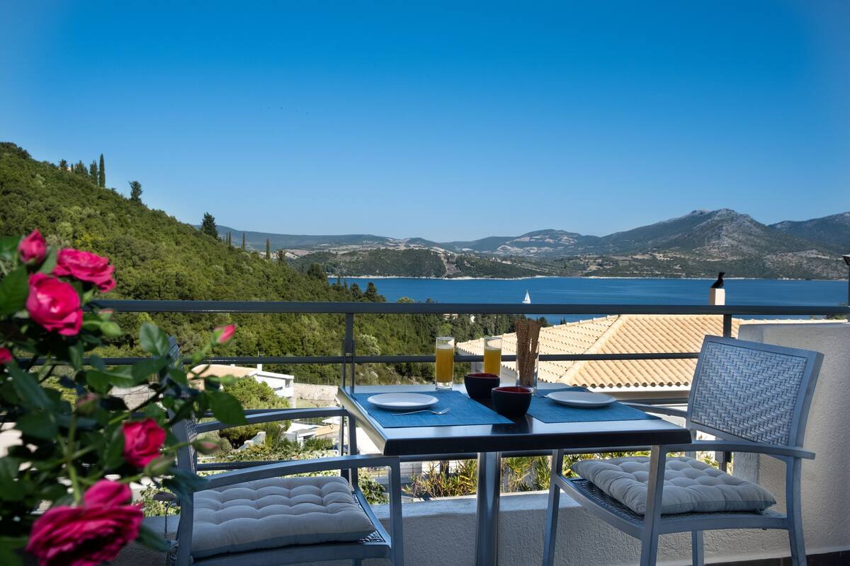 A balcony with a table set for two, overlooking a scenic view of hills and a body of water.