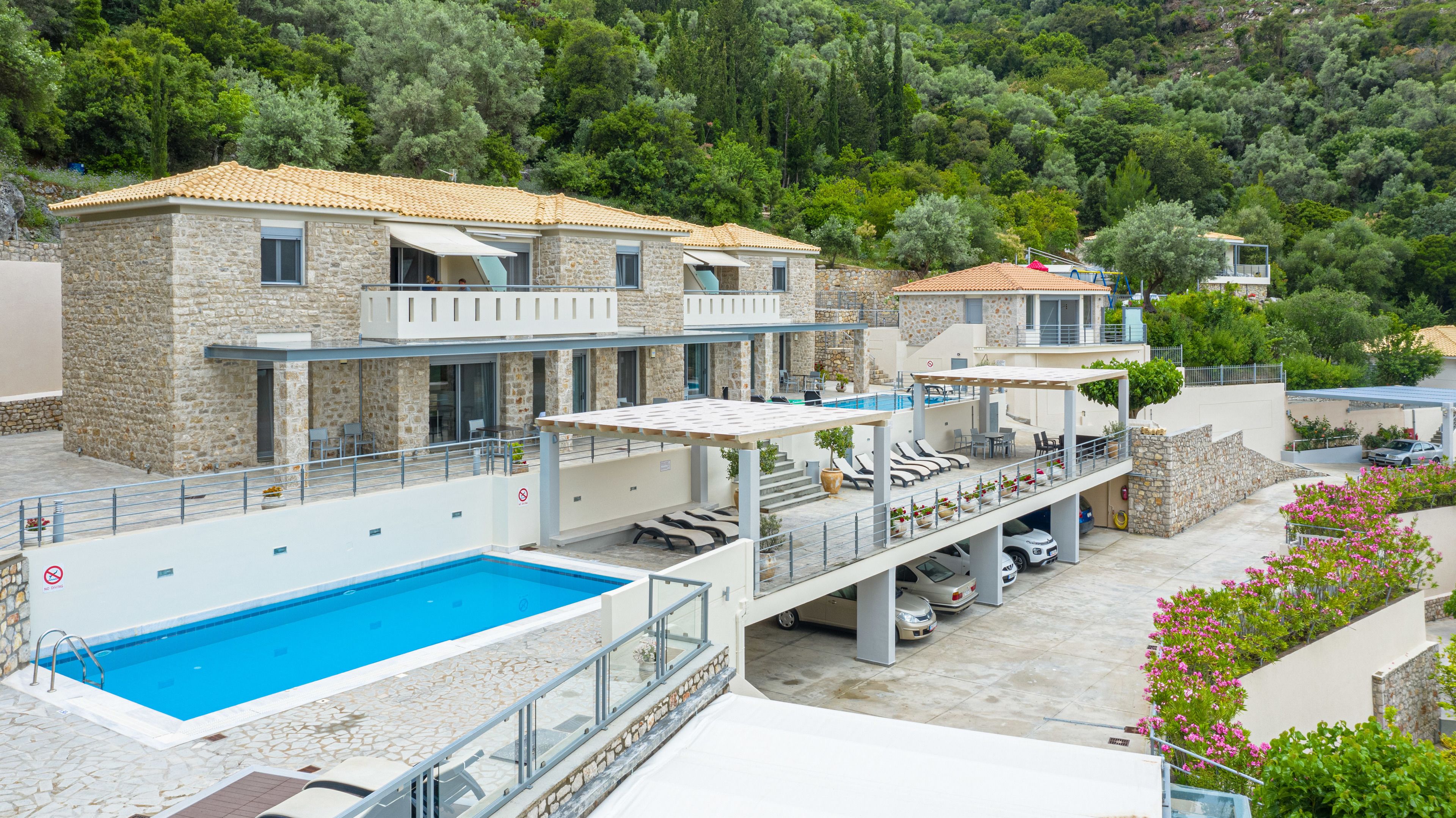A multi-story building with a swimming pool, outdoor seating, and a view of a forested hillside.